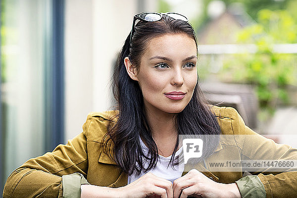 Porträt einer jungen Frau  mit Sonnenbrille im Haar  am Tisch im Freien sitzend