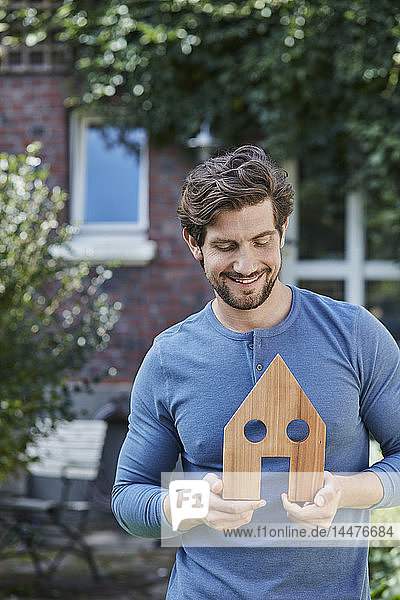 Porträt eines lächelnden Mannes vor dem Modell seines Wohnhauses