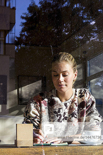 Porträt einer Frau  die in einem Cafe auf einem Notizbuch schreibt