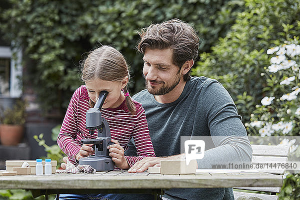 Vater und Tochter benutzen gemeinsam das Mikroskop am Gartentisch