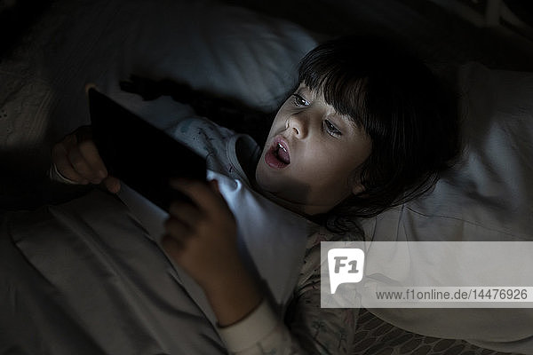 Shocked girl lying in bed using smartphone at night