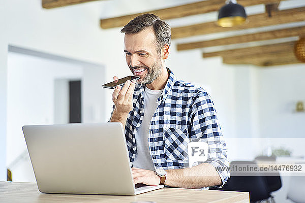 Mann telefoniert  während er zu Hause mit dem Laptop arbeitet