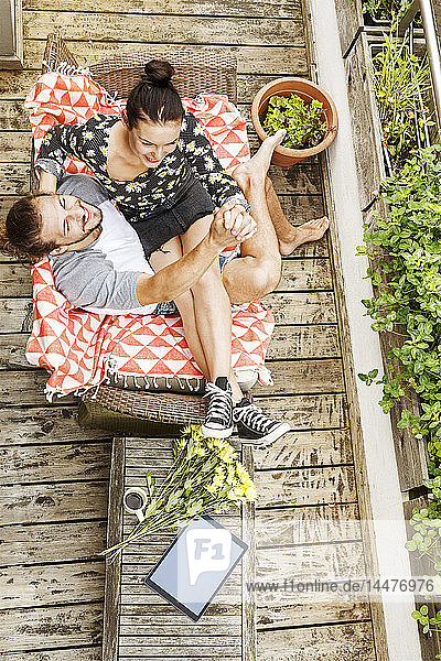 Junges Paar sitzt im Sommer auf seinem Balkon und hält sich an den Händen