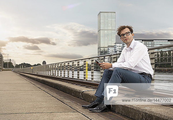 Germany  Berlin  portrait of businessman with smartphone relaxing at River Spree