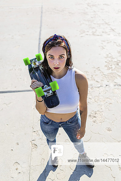 Porträt einer jungen Frau  die stehend ein Skateboard hält