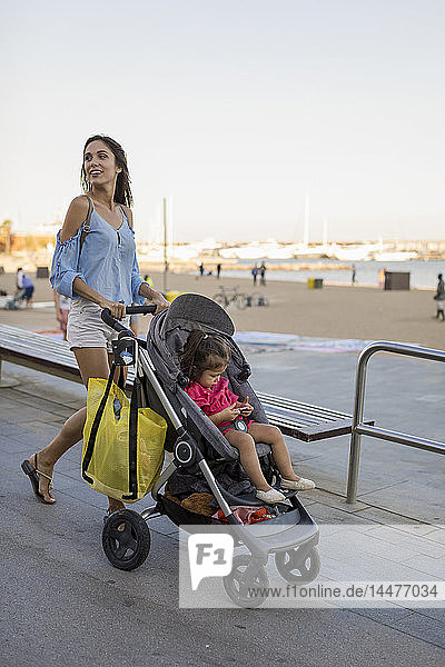 Mother walking at beach promenade with her daughter  sitting in pram