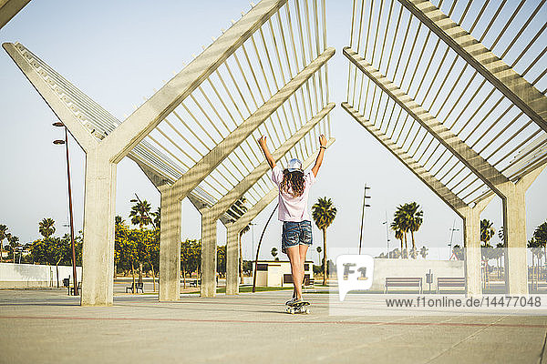 Mädchen auf Skateboard  Arme hochheben  Rückansicht