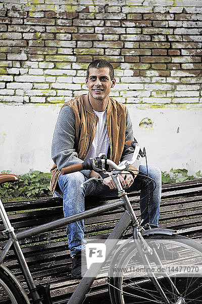 Junger Mann sitzt auf einer Bank neben dem Fahrrad