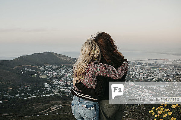 Südafrika  Kapstadt  Kloof Nek  Rückansicht von zwei Frauen  die sich bei Sonnenuntergang umarmen