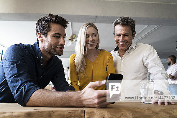 Smiling business team looking at cell phone together in loft office