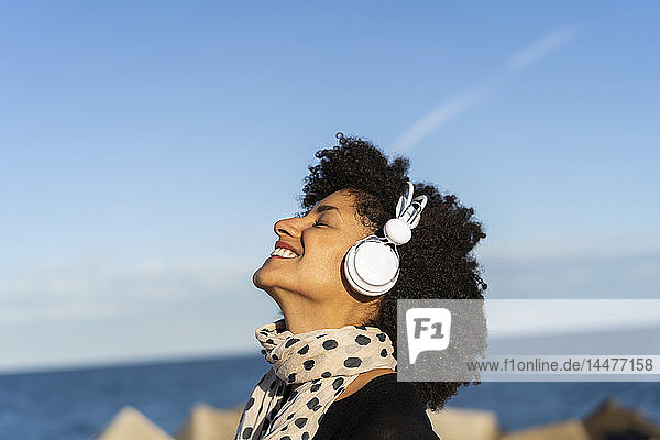 Lächelnde Frau  die in der Nähe des Meeres mit weißen Kopfhörern Musik hört