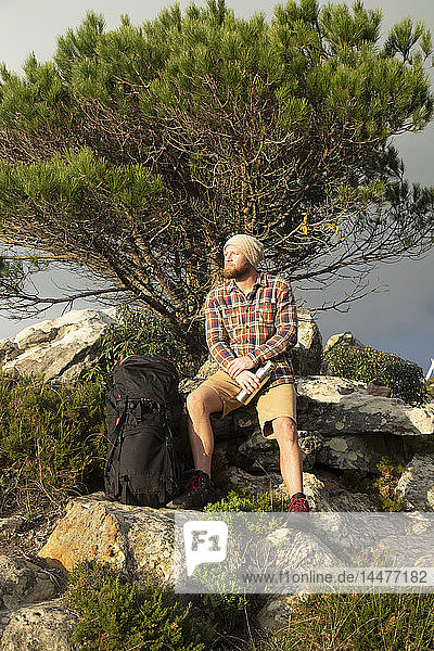 Spanien  Andalusien  Tarifa  Mann auf Wanderung  der auf einem Felsen sitzend eine Pause macht