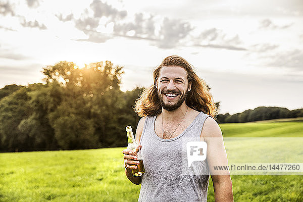 Porträt eines glücklichen Mannes  der Bier in einer ländlichen Landschaft trinkt