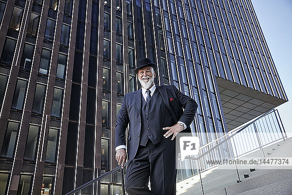 Elegant businessman with bowler hat and walking cane  standing on stairs in the city