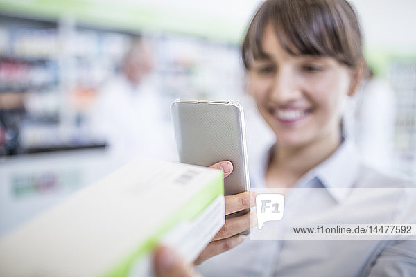 Smiling woman in pharmacy holding smartphone and medicine