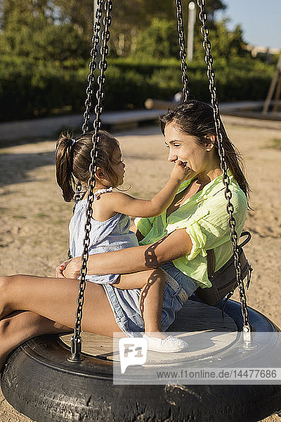 Glückliche Mutter mit Tochter auf Reifenschaukel auf einem Spielplatz
