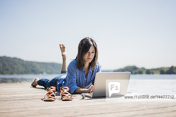 Mature woman working at a lake  using laptop on a jetty