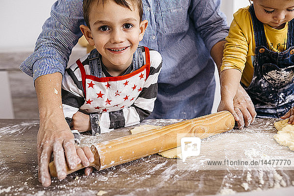 Portrait of happy boy baking cookies together with mother and little sister