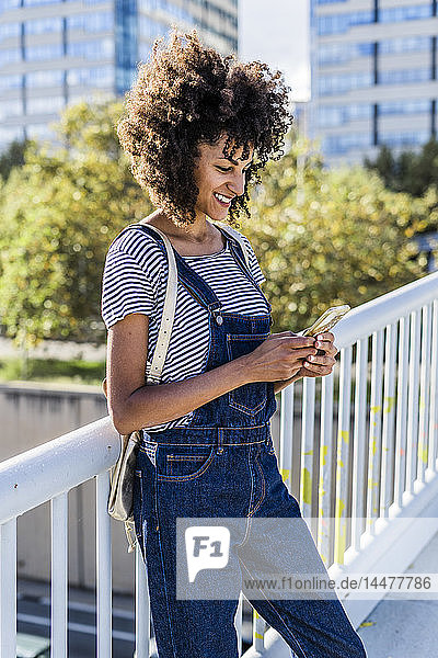 Junge Frau steht auf einer Brücke und benutzt ein Smartphone