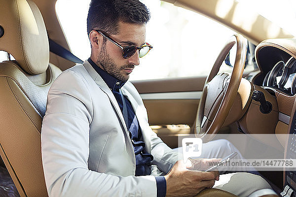 Young businessman sitting in car  using smartphone