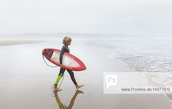 Spanien  Aviles  junger Surfer auf dem Weg zum Wasser