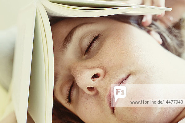 Portrait of young woman sleeping with book on head  close-up