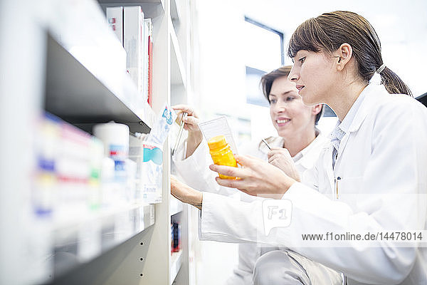 Two pharmacists with pill box at shelf in pharmacy