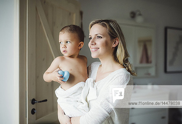 Lächelnde Mutter hält Kleinkind-Sohn im Badezimmer zu Hause