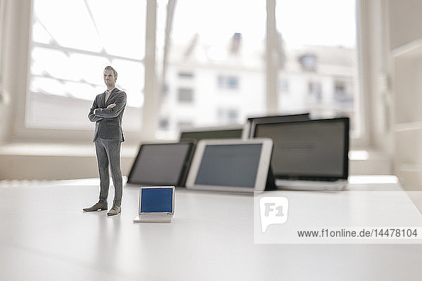 Geschäftsmann-Figur auf Schreibtisch stehend  mobilen Geräten zugewandt