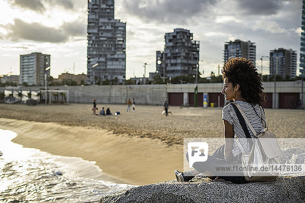 Junge Frau entspannt sich am Strand  sitzt auf Felsen  Rückansicht