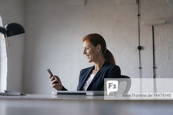 Glückliche Geschäftsfrau mit Handy am Schreibtisch im Büro