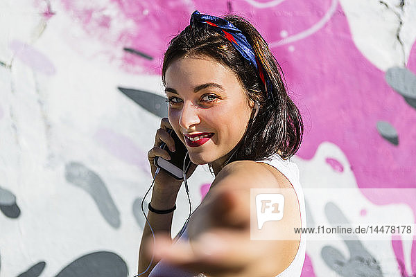Porträt einer lächelnden jungen Frau mit Mobiltelefon und Ohrstöpseln