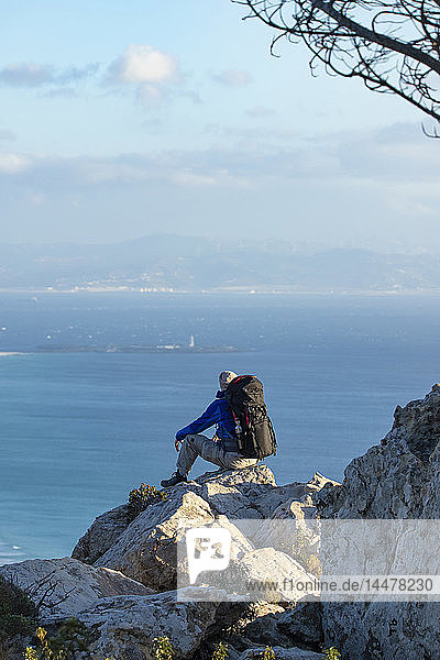 Spain  Andalusia  Tarifa  man on a hiking trip at the coast sitting on a rock looking at view