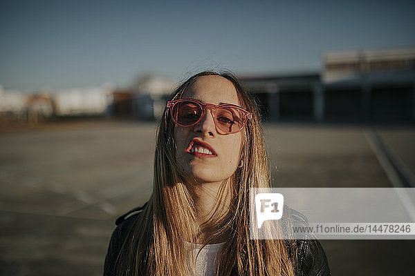 Porträt einer jungen Frau mit trotziger Haltung  die im Freien eine Sonnenbrille trägt