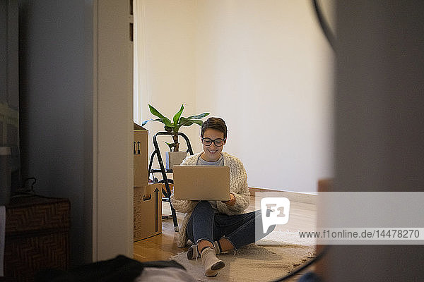 Young woman sitting on floor of her new home  using laptop