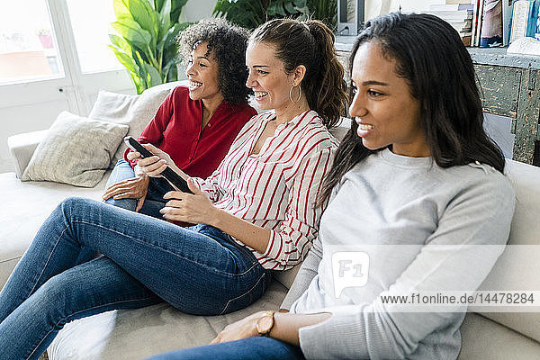 Drei glückliche Frauen sitzen zu Hause auf dem Sofa und sehen fern
