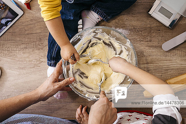 Mother and children preparing dough together  partial view