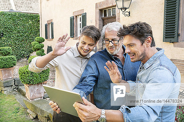Drei Männer unterschiedlichen Alters bei einem Video-Chat per Tablet im Garten