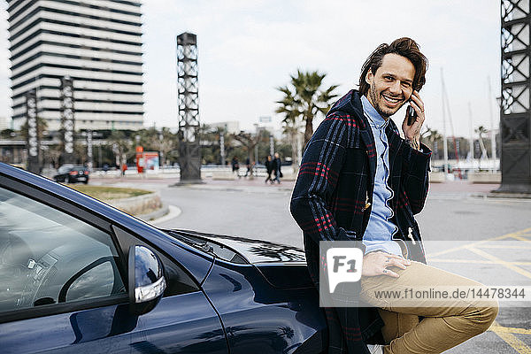 Spanien  Barcelona  lächelnder Mann am Handy vor dem Auto in der Stadt