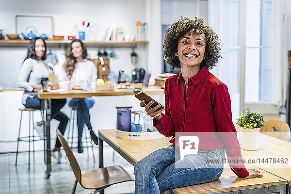 Porträt einer glücklichen Frau mit Handy auf dem Tisch sitzend