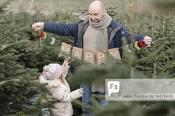 Vater mit Tochter hält Dekoration auf einer Weihnachtsbaumplantage