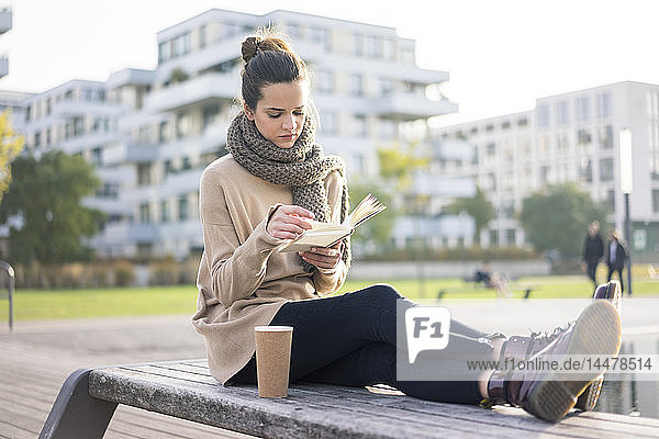 Frau mit Kaffee  um im Herbst auf einer Bank zu sitzen und ein Buch zu lesen
