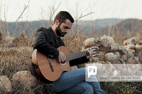 Männlicher Musiker mit Bart beim Gitarrenspiel auf dem Land