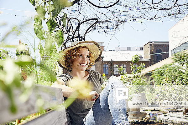 Lächelnde junge Frau mit Strohhut entspannt sich im Stadtgarten
