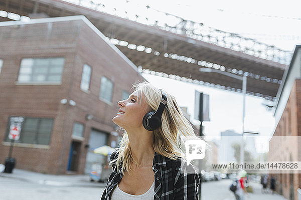 USA  New York City  Brooklyn  glückliche junge Frau  die in der Stadt mit Kopfhörern Musik hört