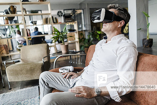Mature man wearing VR glasses sitting on couch in a loft