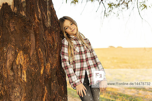 Bildnis eines blonden Mädchens  das sich an einen Baumstamm lehnt