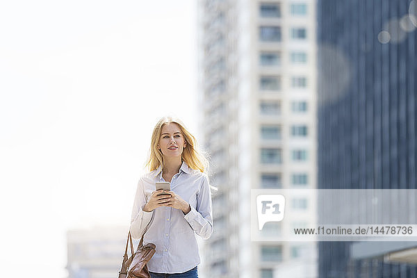 Blonde Frau mit Handtasche und Handy geht durch die Stadt