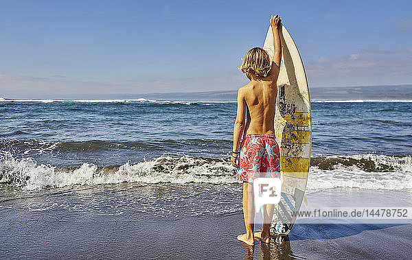 Chile Pichilemu Junge mit Surfbrett am Meer stehend