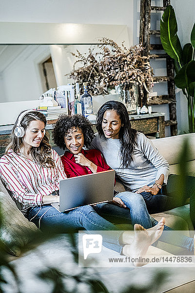 Drei glückliche Frauen mit Laptop auf der Couch sitzend